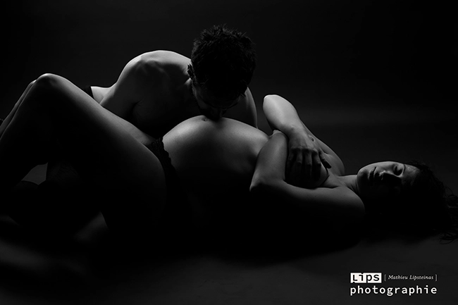 Couple enlacé en clair-obscur sur fond noir, séance grossesse artistique