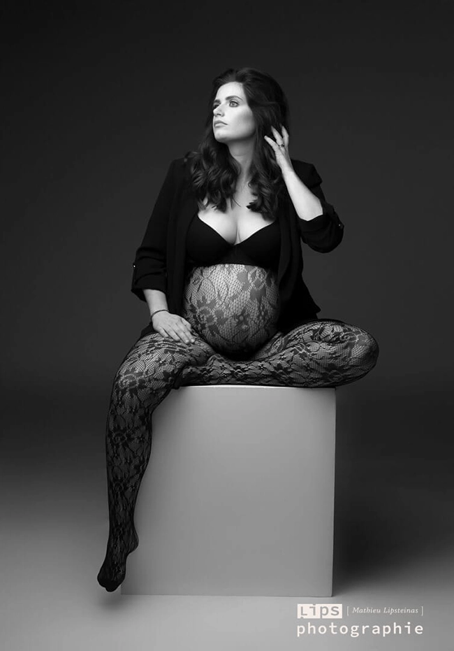 Portrait de studio en noir et blanc d'une femme enceinte assise sur un cube