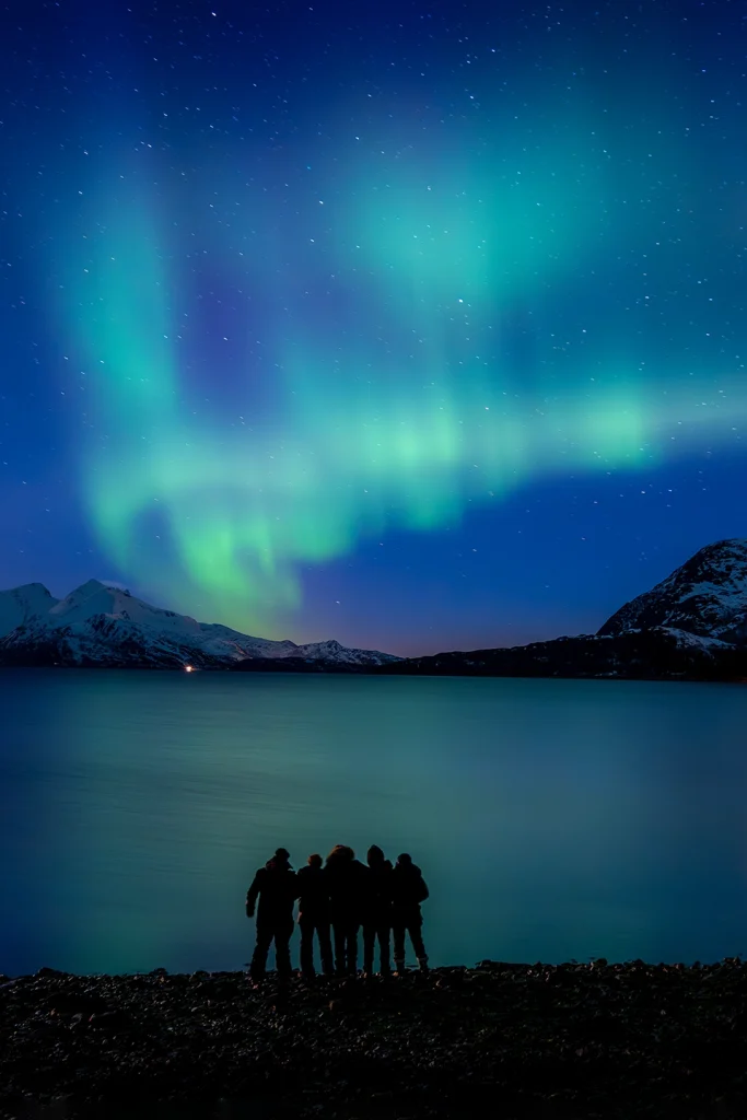 Aurores boréales au-dessus d'un fjord enneigé et silhouettes de voyageurs