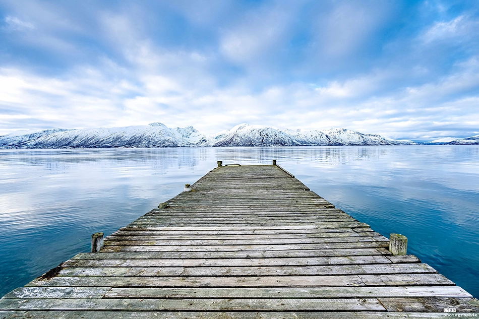 Ponton de bois s'avançant sur un lac devant les montagnes enneigées, Laponie
