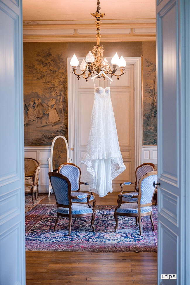 Robe de mariée suspendue dans un salon de château sous un lustre ancien