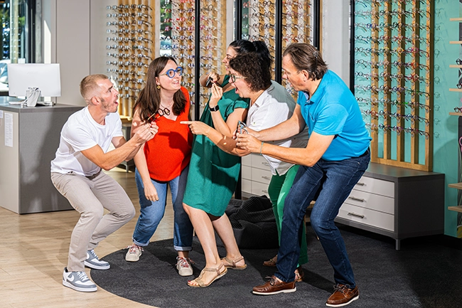 Équipe et clients d'un magasin d'optique posant entre les présentoirs de lunettes