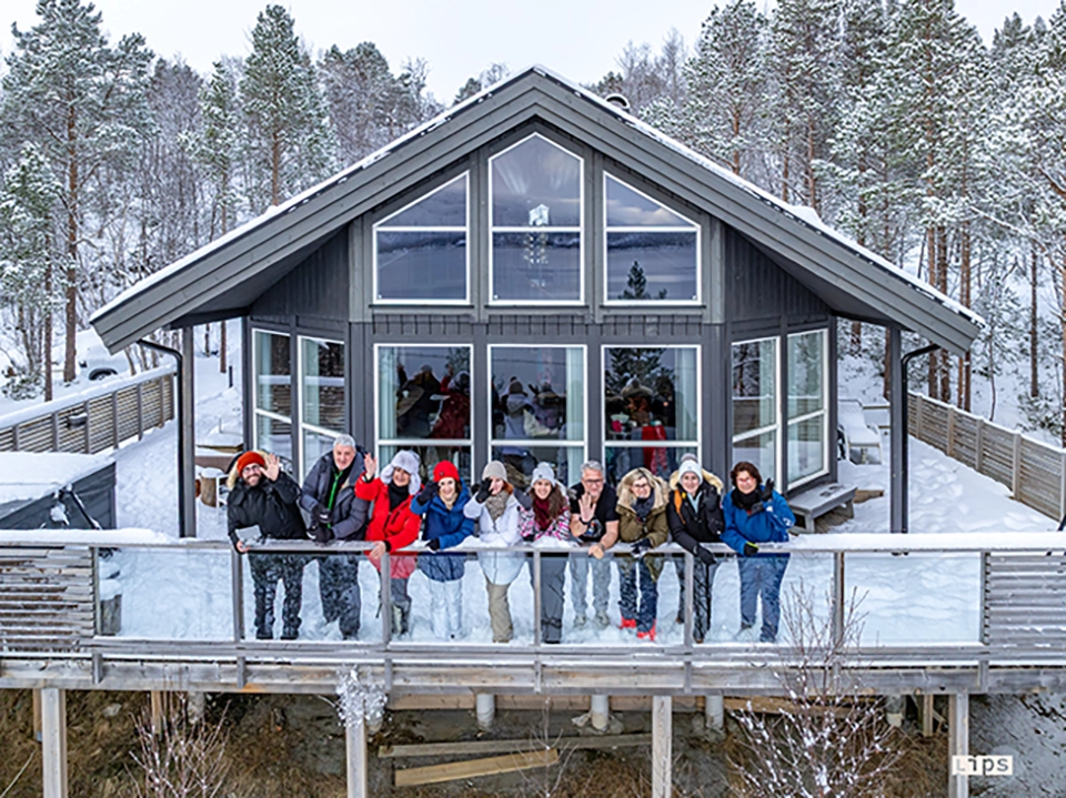 Groupe de voyageurs sur la terrasse d'un chalet enneigé, séjour photo en Laponie
