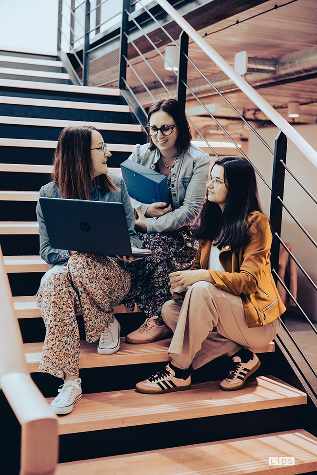 Trois collaboratrices travaillent avec un ordinateur portable dans un escalier de bureaux