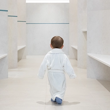 Enfant de dos en combinaison blanche dans un couloir clair, photographie d'ambiance