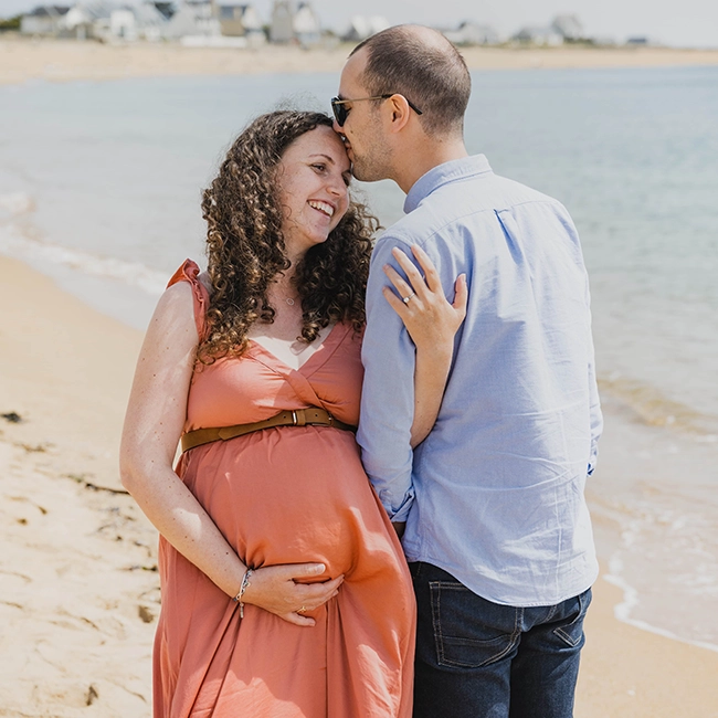 Couple attendant un enfant sur la plage, future maman en robe corail, séance grossesse
